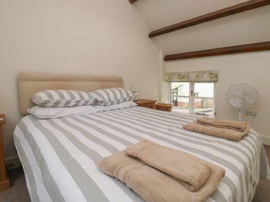 A bedroom with a double bed striped bedding folded towels bedside tables window and a fan at Bantam Cottage Little Woodford near Ottery St Mary