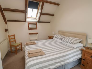 A bedroom with a double bed with striped bedding under a skylight window at Bantam Cottage in Little Woodford near Ottery St Mary