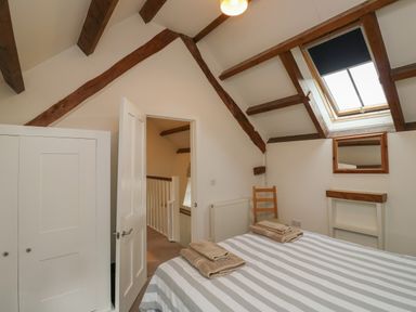 A bedroom with a bed striped bedding towels on bed a wooden chair a skylight window and wooden beams at Bantam Cottage in Little Woodford near Ottery St Mary