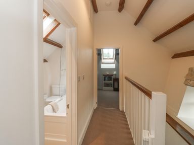 A hallway with a bathroom on the left and a room with a skylight window and bookshelf at Bantam Cottage in Little Woodford near Ottery St Mary