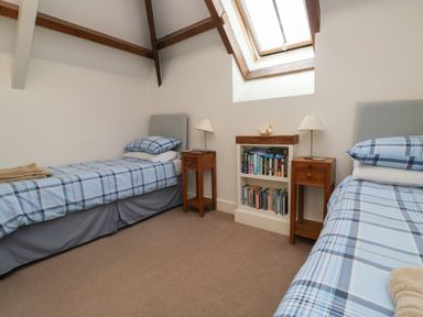 A bedroom with two single beds with blue plaid bedding two wooden nightstands a bookshelf and a skylight window at Bantam Cottage in Little Woodford near Ottery St Mary