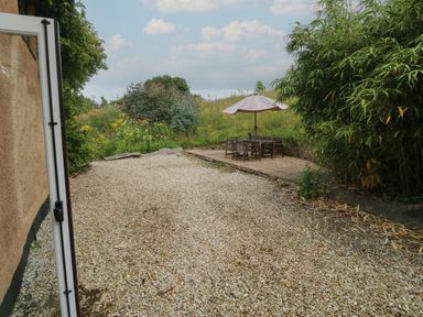 An outdoor patio area with gravel ground and a seating area with table umbrella at Bantam Cottage in Little Woodford near Ottery St Mary