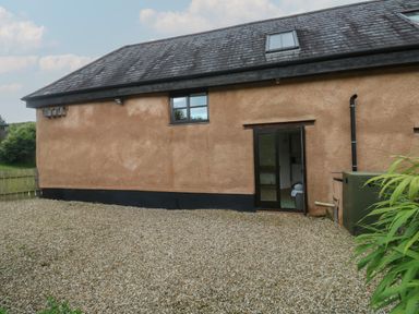 Exterior of a building with a tiled roof gravel ground and an open door showing an interior room with a sink at Bantam Cottage in Little Woodford near Ottery St Mary