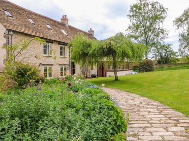 A stone pathway leading to a stone house with a garden and trees at Tickmorend Farm in Nailsworth