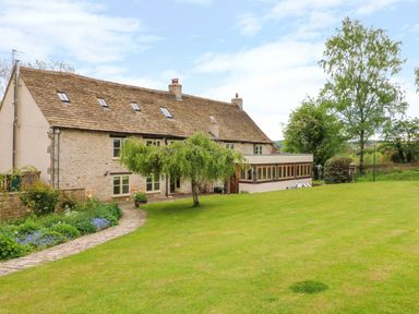 A large stone house with a garden and trees at Tickmorend Farm in Nailsworth