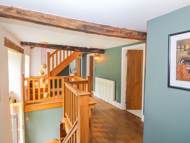 A stairway landing with wooden railings wooden doors a radiator a hanging light fixture and exposed wooden beams at Tickmorend Farm in Nailsworth