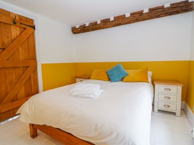 A bedroom with a wooden door a bed with white bedding and yellow and blue pillows and two bedside tables at Tickmorend Farm in Nailsworth
