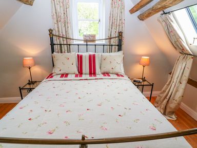 A bedroom with a bed with floral bedding and pillows two bedside tables with lamps and floral curtains at Tickmorend Farm in Nailsworth