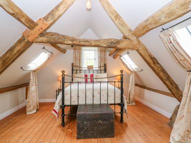 A bedroom with a metal bed frame wooden chest wooden beams and curtains at Tickmorend Farm in Nailsworth