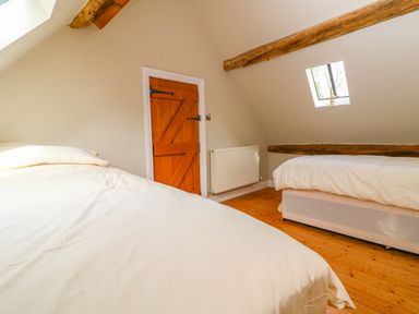 A bedroom with two single beds wooden door exposed wooden beams and a skylight window at Tickmorend Farm in Nailsworth
