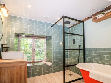 A bathroom with a wooden vanity and a white sink a glass shower enclosure green tiled walls and a red bathtub at Tickmorend Farm in Nailsworth