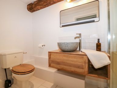 A bathroom with a toilet and a wooden vanity with a round stone sink and a mirror above at Tickmorend Farm in Nailsworth
