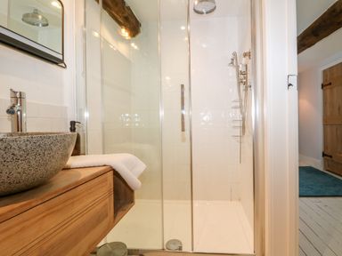 A bathroom with a glass shower enclosure a stone sink on a wooden vanity and a wooden door visible through a hallway at Tickmorend Farm in Nailsworth