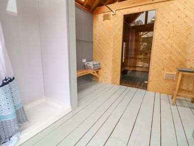 An indoor area with a shower cabin a wooden bench with folded towels and a glass door leading to a wooden room at Tickmorend Farm in Nailsworth