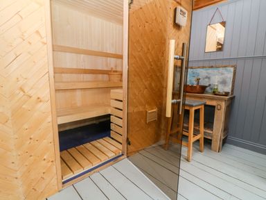 A wooden sauna room with benches and a bucket next to a wooden table with a copper sink and stool at Tickmorend Farm in Nailsworth