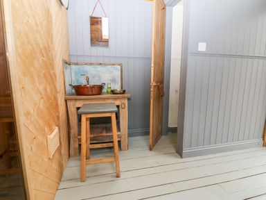 A small wooden table with a copper basin and soap dispenser with a wooden stool in a room with wooden paneled walls at Tickmorend Farm in Nailsworth
