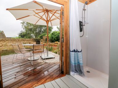 A shower area with a curtain next to a wooden deck with a table four chairs and a large umbrella at Tickmorend Farm in Nailsworth