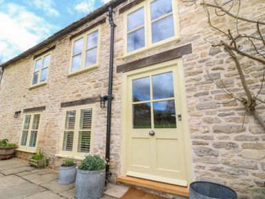 A stone house with cream windows and door with outdoor plants in metal pots at Tickmorend Farm in Nailsworth