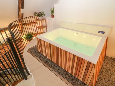 An indoor bathtub with wooden paneling near a black metal spiral staircase at Tickmorend Farm Nailsworth
