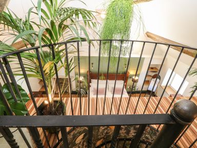 A bedroom with a wooden bed and green wall seen from a balcony with black metal railing and plants at Tickmorend Farm in Nailsworth