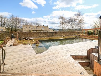 An outdoor area with a wooden deck and a natural swimming pond surrounded by a stone wall at Tickmorend Farm in Nailsworth