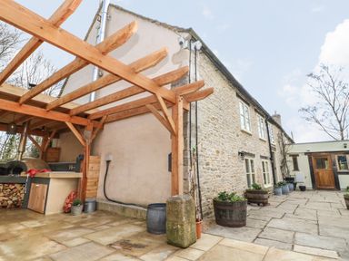 An outdoor patio area with stone flooring a wooden pergola and a stone building with potted plants at Tickmorend Farm Nailsworth