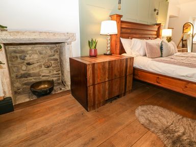 A bedroom with a wooden bed and nightstand with lamps and a plant next to a fireplace at Tickmorend Farm Nailsworth