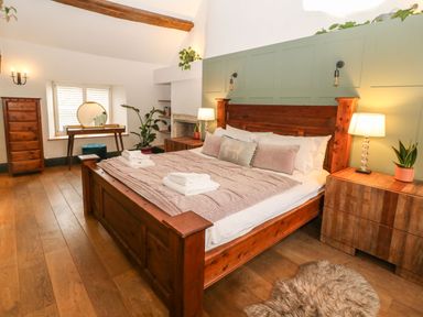 A bedroom with a wooden bed a dressing table with a round mirror and plants at Tickmorend Farm in Nailsworth