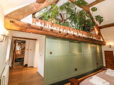 An interior room with green paneled wall wooden ceiling beams plants on loft and wooden furniture at Tickmorend Farm in Nailsworth