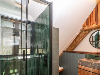 A bathroom with a glass shower enclosure tiled in green and a stone sink with wooden accents at Tickmorend Farm in Nailsworth