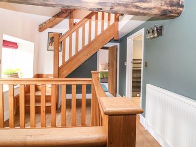 A hallway with wooden staircase and railing with a window and doors leading to other rooms at Tickmorend Farm in Nailsworth