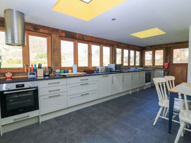 A kitchen with white cabinets black countertops multiple windows and a dining table with chairs at Tickmorend Farm in Nailsworth