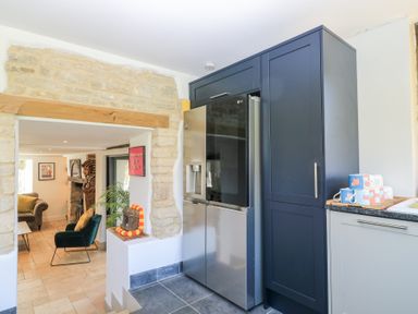 A kitchen area with a stainless steel refrigerator next to dark blue cabinets and mugs on a counter at Tickmorend Farm in Nailsworth