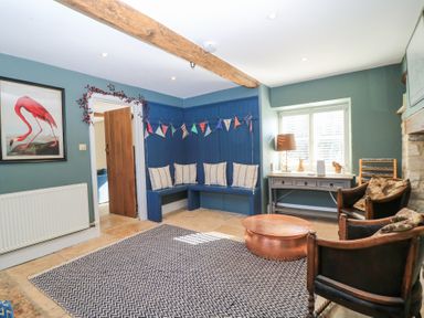 A sitting room with blue corner bench seating cushions wooden chairs a copper coffee table and a framed flamingo picture at Tickmorend Farm in Nailsworth