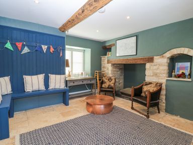 A living room with blue bench seating cushions wooden table armchairs fireplace and exposed beams at Tickmorend Farm in Nailsworth