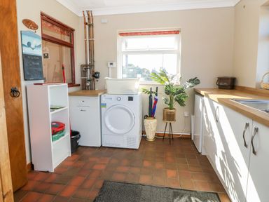 A utility room with a washing machine a basket plants and cabinets at Buarthau Cottage in Llanrug