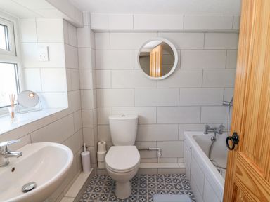 A bathroom with a toilet sink bathtub mirror and a wooden door at Buarthau Cottage in Llanrug