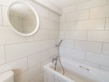 A bathroom with a bathtub a round mirror and a toilet at Buarthau Cottage in Llanrug