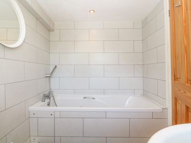 A bathroom with a bathtub shower fixtures a round mirror and a wooden door at Buarthau Cottage in Llanrug