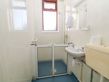 A bathroom with a shower, sink, toilet, and frosted window at Buarthau Cottage in Llanrug