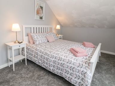 A bedroom with a double bed, bedside tables with lamps, and folded towels at Buarthau Cottage in Llanrug