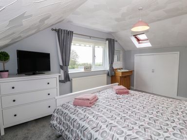 A bedroom with a bed a dresser a television a window with curtains a sink and built in cupboards at Buarthau Cottage in Llanrug