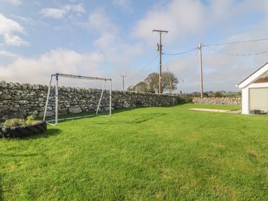 A grassy yard with a soccer goal and stone walls near a white building at Buarthau Cottage in Llanrug