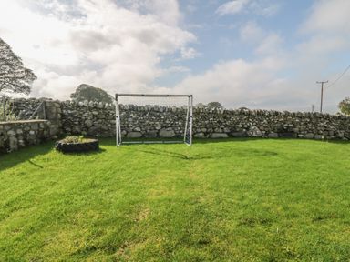 A small grass field with a soccer goal and a stone wall surrounding it at Buarthau Cottage in Llanrug
