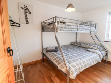 A bedroom with a metal bunk bed with plaid bedding a giraffe picture on the wall and a wooden floor at Buarthau Cottage in Llanrug