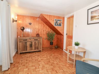 A room with wooden paneled walls and parquet floor with a wooden cabinet a round wooden side table with a plant and a wooden door at Buarthau Cottage in Llanrug