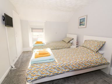 A bedroom with two single beds with patterned bedding and folded towels a wall-mounted television and a small window at Buarthau Cottage in Llanrug