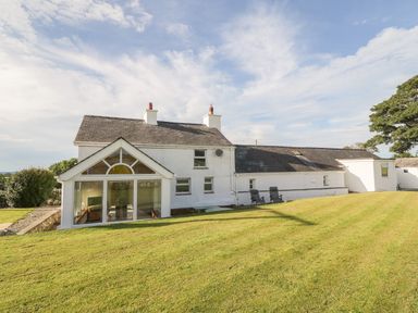 A white house with a glass sunroom and two black chairs on a lawn at Buarthau Cottage in Llanrug