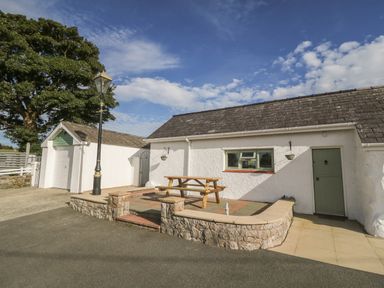An outdoor patio with a picnic table stone walls and a green door at Buarthau Cottage in Llanrug