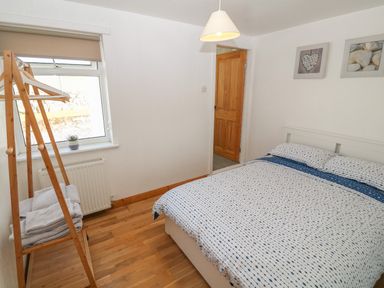 A bedroom with a bed a wooden door a window and a wooden clothes rack with towels at Buarthau Cottage Llanrug